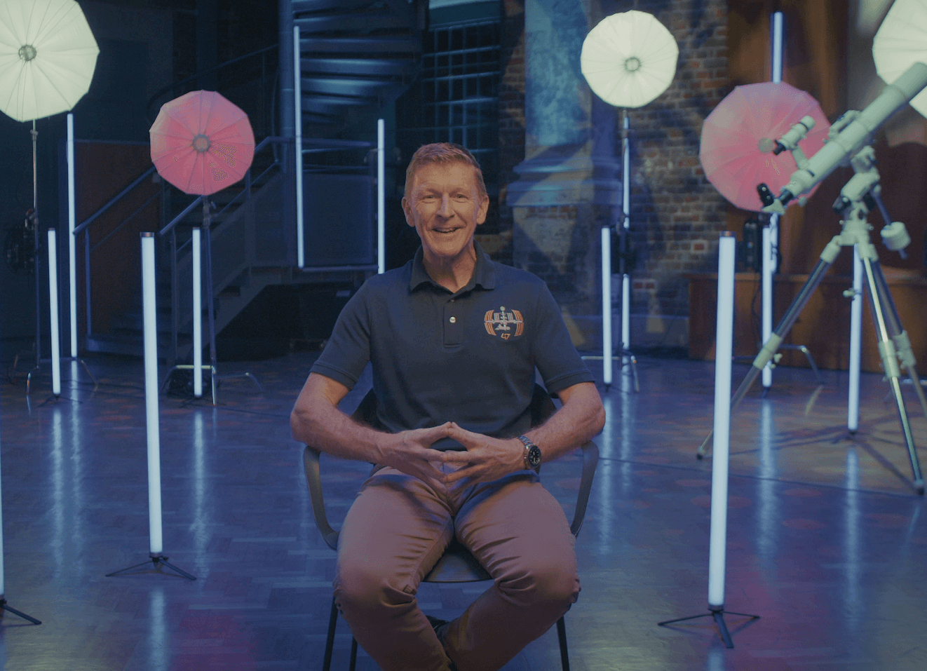 Tim Peake sitting towards the camera surrounded by space themed lighting