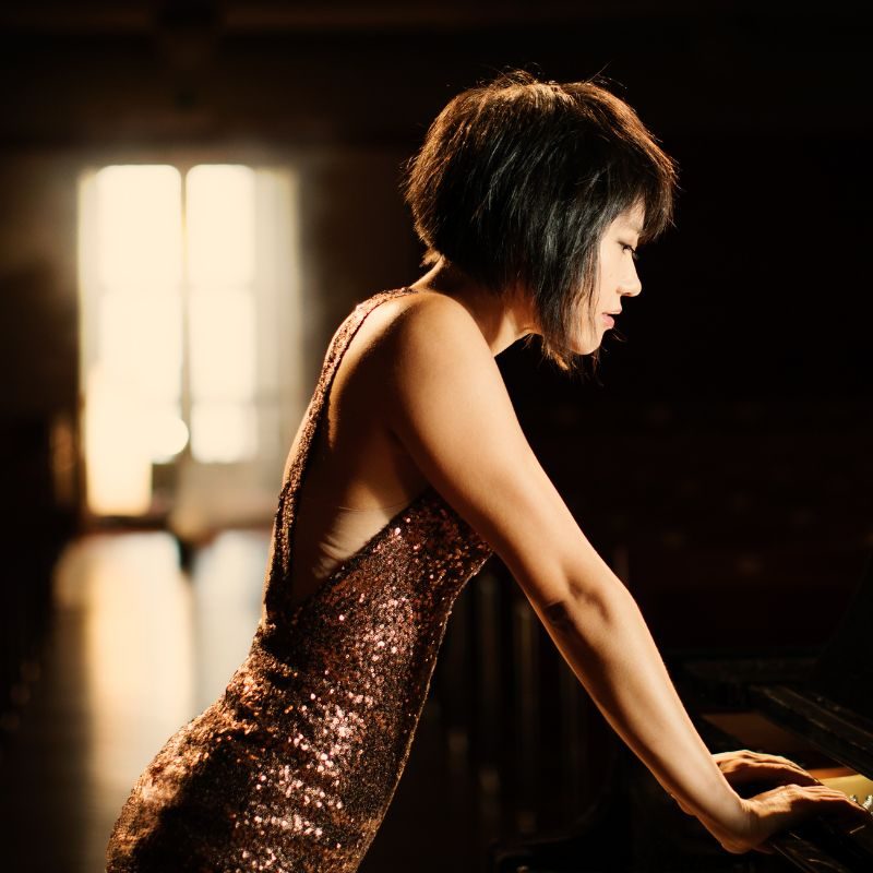 Yuja Wang, side on to the camera, leaning on a piano