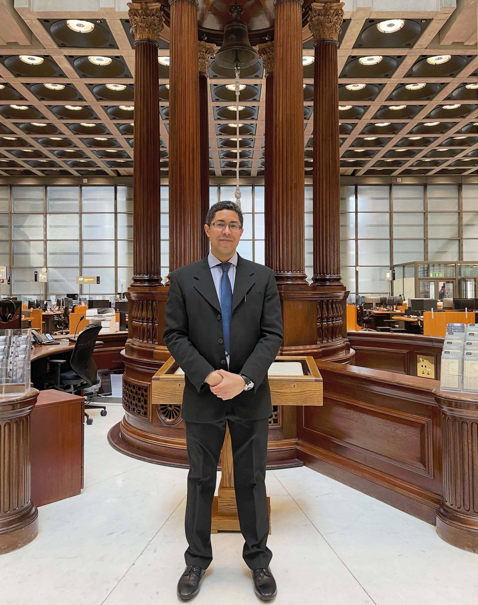 Photo of David Önaç standing in front of the 'Lutine bell' in the Lloyd's of London headquarters