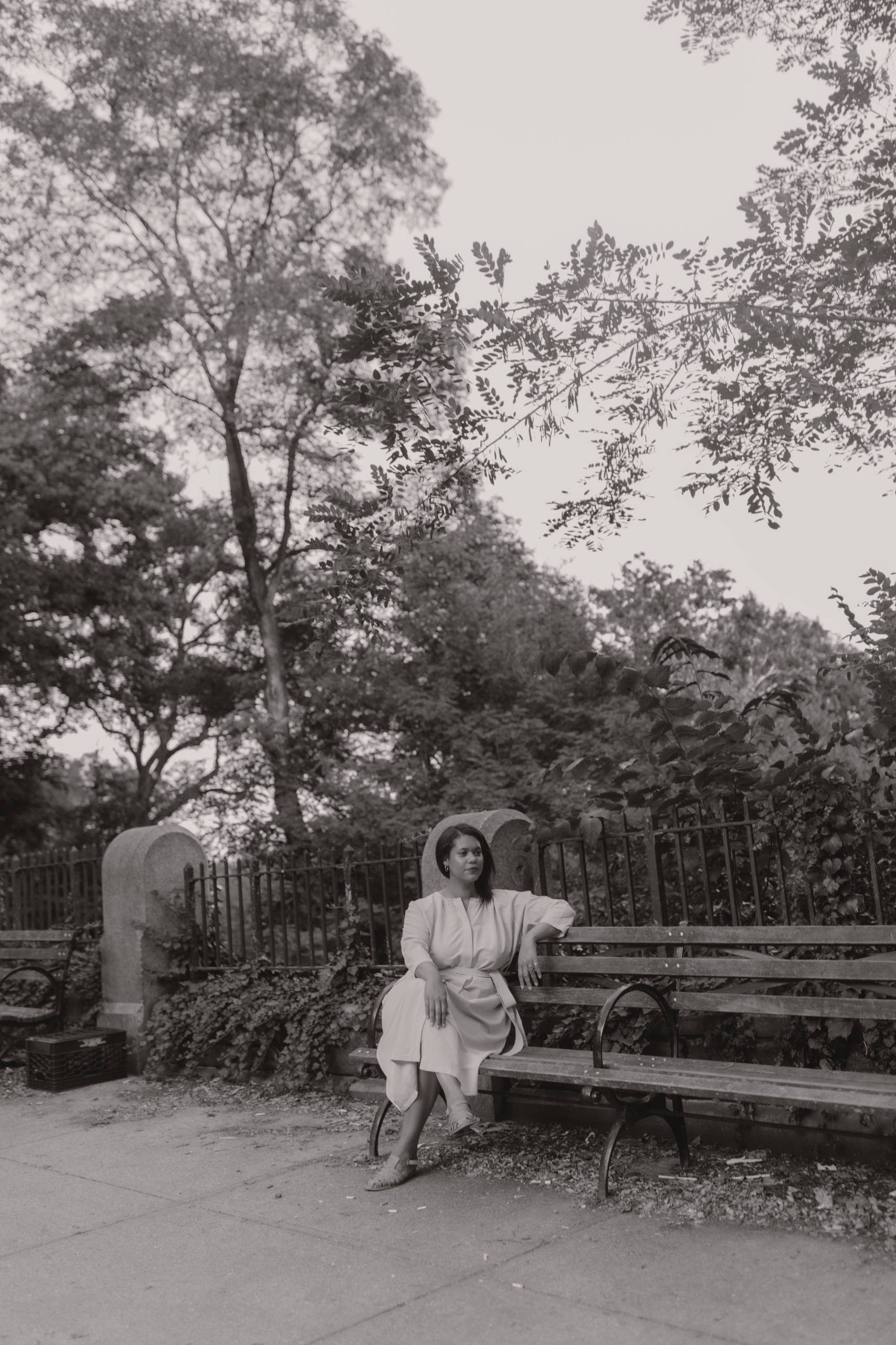 Black and white image of Hannah Kendall on a bench behind a tree-lined sky